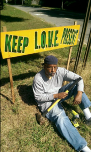 Naim Muslim sitting on the ground in front of a keep love present sign he just put up.
