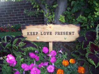 This is a picture of a garden. In the center of it there is a sign that reads Keep Love Present